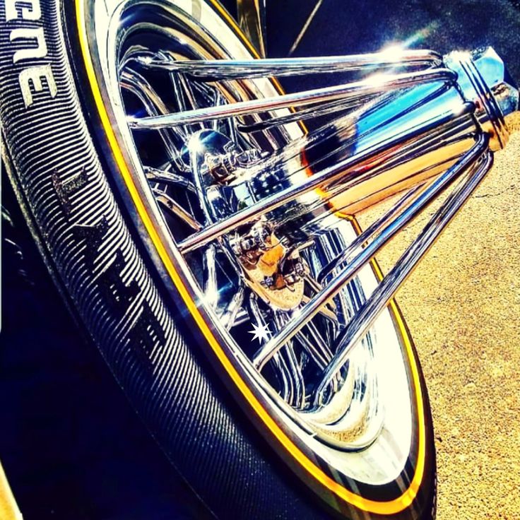 Chrome 30-spoke swanga wire wheel poking out from a slab, wrapped in a gold-stripe vogue tire